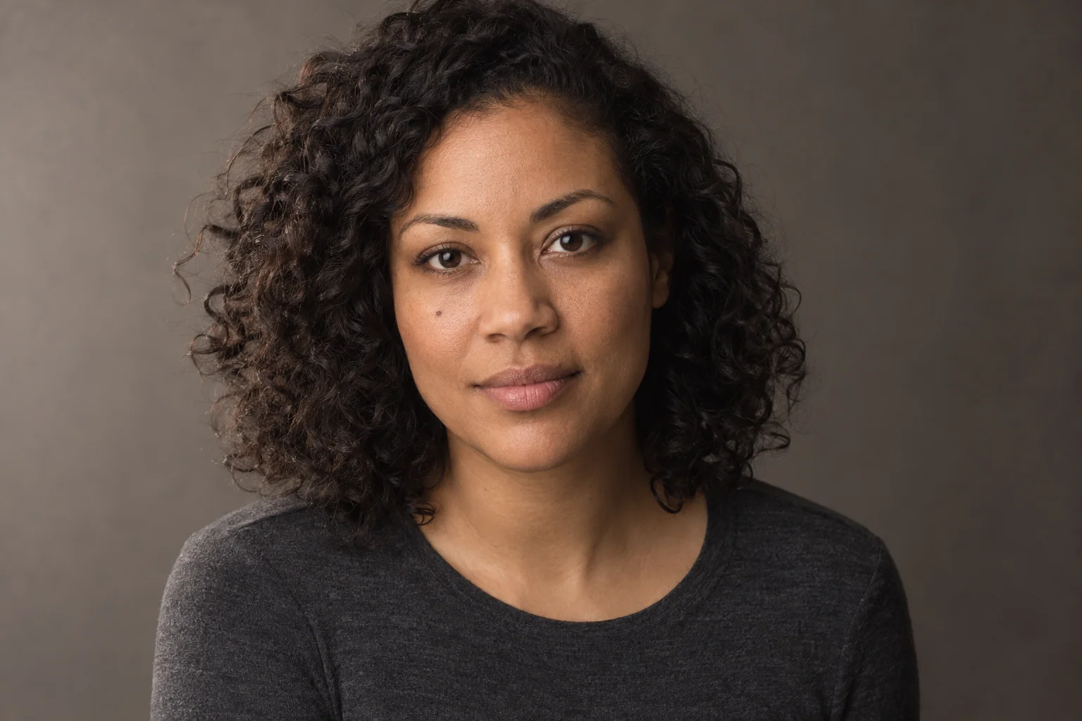 A fictional curly-haired woman lit softly from camera-left against a neutral background.